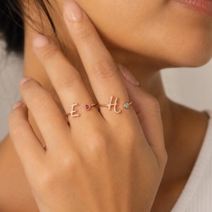 Può includere: Due anelli aperti in oro rosa con le lettere corsive E e H. L'anello con la lettera E è impreziosito da una piccola pietra preziosa rotonda rosa, mentre l'anello con la lettera H presenta una piccola pietra rotonda azzurra all'estremità.