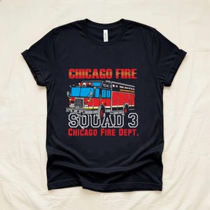 Pode incluir: Uma t-shirt preta de manga curta com um gráfico de um camião de bombeiros vermelho e branco. O texto diz CHICAGO FIRE, SQUAD 3 e CHICAGO FIRE DEPT. em letras vermelhas e brancas. O design está centrado no peito da peça de vestuário.