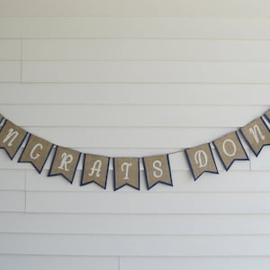 May include: A burlap banner with navy blue trim and white lettering that reads "Congrats Donny".