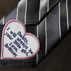 May include: A black and white striped tie with a pink heart-shaped patch that says "Daddy I will always be your little girl, Love, Britney".