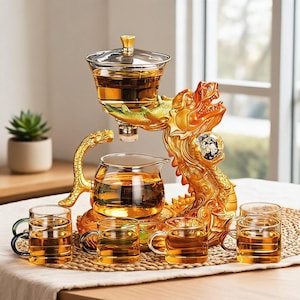 Puede incluir: Un juego de té de cristal con una base de escultura de dragón dorado que sostiene un infusor y una tetera de cristal transparente. El set incluye cuatro tazas pequeñas de cristal con asas de colores, llenas de té ámbar sobre una esterilla.