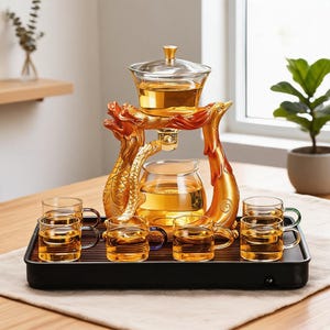 Puede incluir: Un juego de té de cristal con un soporte dorado de dragón y fénix que sostiene una tetera sobre una jarra de cristal. Seis tazas pequeñas de cristal con asas de colores están dispuestas sobre una bandeja negra rectangular con listones.