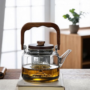 May include: A clear glass teapot featuring a dark wood lid and a matching arched wooden handle. The teapot contains a central glass infuser chamber and is filled with a golden-colored liquid. It has a short, angled spout on the right side.