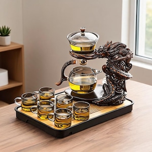 May include: A tea set featuring a glass teapot and six small glass cups filled with golden tea. The set includes a dark brown, sculpted dragon-shaped stand that supports the teapot and a lid, all arranged on a rectangular bamboo serving tray.