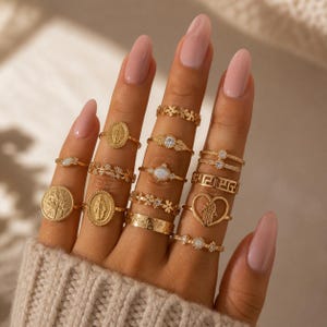 以下が含まれることがあります： 指に飾られた金色の指輪のコレクション。指輪には、花柄、宝石、宗教的なモチーフなど、さまざまなデザインが施されています。指輪はさまざまなサイズとスタイルで、重ね着したような外観になっています。