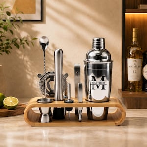 Könnte beinhalten: Ein Cocktail-Shaker-Set aus Edelstahl mit einem Bambusständer. Der Shaker ist mit einem schwarzen Monogramm mit dem Namen MATTHEW versehen. Das Set enthält einen Messbecher, einen gedrehten Barlöffel, ein Barsieb, einen Stößel, einen Ausgießer und eine Zange.