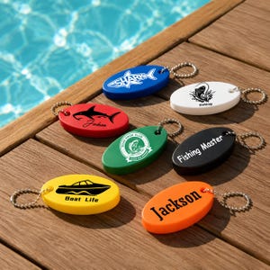 Puede incluir: Una colección de siete llaveros flotantes de espuma con forma ovalada en azul, blanco, rojo, verde, negro, amarillo y naranja. Cada llavero incluye una cadena de bolas de metal y gráficos impresos únicos, con textos como Shark, Fishing, Bass Hook Club, Fishing Master, Boat Life y Jackson.