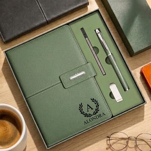 May include: A sage green stationery gift set in a rectangular box, featuring a leather-textured notebook with a magnetic closure, a matching ballpoint pen, and a metal clip. The notebook cover is embossed with a laurel wreath, the letter A, and the name ALONDRA.