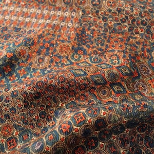 May include: Close-up of a patterned fabric with a vintage aesthetic. The design features repeating circular and geometric shapes in shades of blue, orange, and brown. The fabric has a textured appearance, suggesting a woven material.