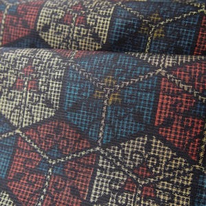 May include: A textile fabric featuring a repeating geometric pattern of interconnected hexagons in shades of deep blue, muted red, and cream. The surface displays a fine, woven grid texture throughout, with each hexagonal shape containing intricate, small-scale cross-hatched details in contrasting colours.