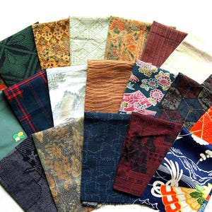 May include: A collection of rectangular fabric swatches arranged in a fan shape, featuring a variety of patterns including floral, geometric, plaid, and landscape designs in colors such as red, blue, green, brown, black, and gold.