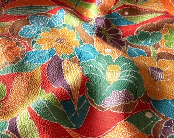 May include: A textured fabric featuring a vibrant floral pattern with a red background. The design includes stylised flowers and leaves in shades of yellow, green, blue, orange, and purple. The material has a distinct crinkled, pebbled surface texture.