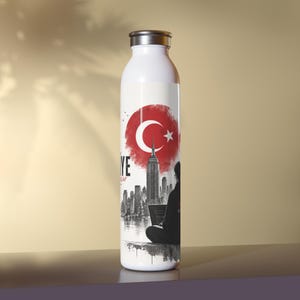 May include: White stainless steel water bottle with a silver cap. The bottle features a design with the Turkish flag, the New York City skyline, and a person using a laptop. The word "YE" is also visible.