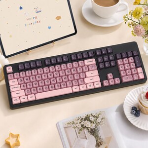 May include: A mechanical keyboard with a black frame, featuring a mix of dark purple function keys and light pink alphanumeric keys. The layout includes a full numeric keypad on the right side, with standard QWERTY lettering printed in black on each keycap.