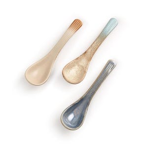 Op de afbeelding: Drie keramische lepels in verschillende kleuren: beige met een bruin handvat, gespikkeld bruin met een lichtblauw handvat en blauw met een donkerder blauw handvat. Elke lepel heeft een lange, slanke steel en een afgeronde kom, perfect voor het serveren van kleine porties.