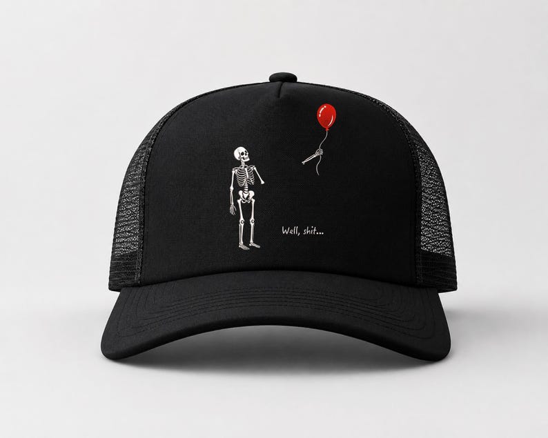 May include: A black trucker hat featuring a graphic of a white skeleton looking up at a red balloon tied to a detached skeletal hand. The text "Well, shit..." is printed in white below the skeleton on the front panel of the cap.