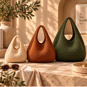 Könnte beinhalten: Drei Taschen im Hobo-Stil aus gehäkeltem Garn in Creme, Rostorange und Dunkelgrün. Jede Tasche verfügt über einen einzelnen integrierten Griff und ein strukturiertes Rippenmuster. Die Taschen sind in einer Reihe von klein nach groß angeordnet.