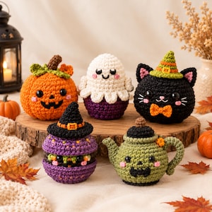 Könnte beinhalten: Eine Sammlung von fünf gehäkelten Halloween-Figuren, darunter ein orangefarbener Kürbis, ein weißes Gespenst, eine schwarze Katze mit grünem Hut, ein lila Glas mit Hexenhut und eine grüne Teekanne, alle mit gestickten Gesichtern und Details.