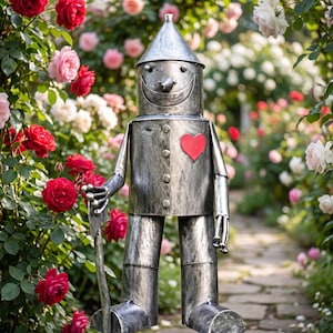 Könnte beinhalten: Eine metallisch silberfarbene Roboterfigur mit einem kegelförmigen Hut, einem breiten lächelnden Mund und einem auffälligen roten Herz auf der Brust. Die Figur hat einen zylindrischen Rumpf, bewegliche Arme und hält ein langes, dünnes Werkzeug.