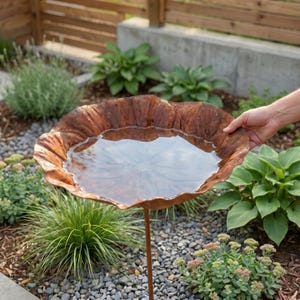 Pu&ograve; includere: Un bagno per uccelli color rame con un'ampia vasca a forma di foglia dai bordi smerlati, riempita d'acqua limpida. La vasca &egrave; sostenuta da un sottile stelo metallico verticale, creando una struttura a ciotola aperta e poco profonda.