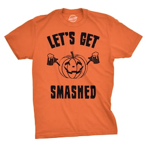 Puede incluir: Camiseta naranja con un gráfico de calabaza negra y el texto "Let's Get Smashed".