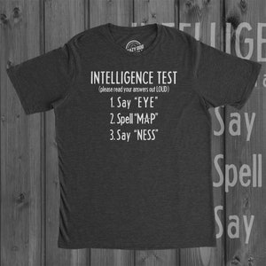 May include: A dark gray t-shirt with white text that reads "INTELLIGENCE TEST (please read your answers out LOUD) 1. Say "EYE" 2. Spell "MAP" 3. Say "NESS""