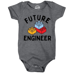 May include: A dark heather gray short-sleeve baby bodysuit featuring the black text FUTURE ENGINEER and a graphic of three interlocking building blocks in yellow, light blue, and red. The garment has a crew neckline and three metal snaps.