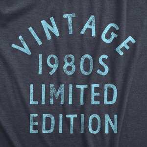 May include: Dark blue t-shirt with the words "VINTAGE 1980s LIMITED EDITION" in light blue, distressed font. The text is arranged in an arch and stacked vertically.