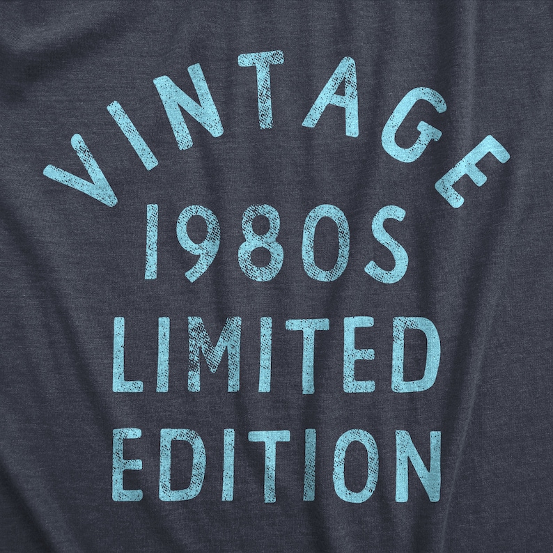 May include: Dark blue t-shirt with the words "VINTAGE 1980s LIMITED EDITION" in light blue, distressed font. The text is arranged in an arch and stacked vertically.