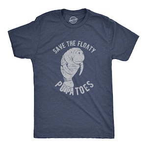 May include: A navy blue short-sleeve t-shirt featuring a distressed white graphic of a manatee in the center. The text above the manatee reads "SAVE THE FLOATY" and the text below reads "POTATOES" in a distressed white, capitalized font.