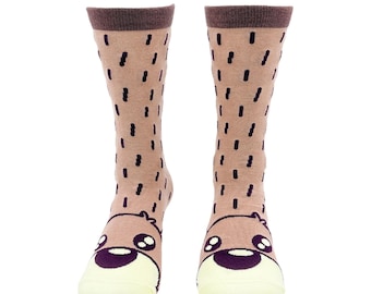 May include: A pair of crew-length socks in a light brown color featuring a dark brown cuff at the top. The socks are decorated with a pattern of small dark brown vertical dashes and a cartoon animal face on the toe area with large eyes.
