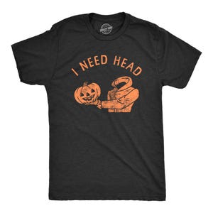 May include: Dark gray t-shirt with the text "I NEED HEAD" in orange. The graphic shows a headless figure holding a carved pumpkin. The shirt is a Halloween-themed design.