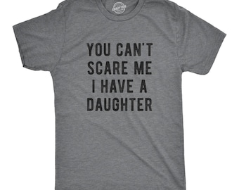 Puede incluir: Una camiseta de manga corta en color gris oscuro jaspeado con el texto negro YOU CAN'T SCARE ME I HAVE A DAUGHTER impreso en una fuente negrita sin remates en el pecho. La prenda tiene cuello redondo y un corte estándar y casual.