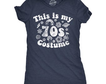 Puede incluir: Una camiseta azul marino de manga corta con texto blanco desgastado impreso que dice This is my 70s Costume. El gráfico incluye iconos de un arcoíris, flores, un planeta, un símbolo de la paz, un hongo y cerezas en un estilo retro.