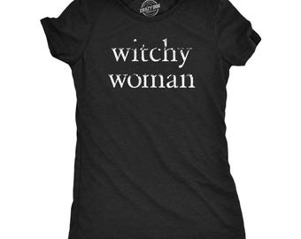 以下が含まれることがあります： クルーネックの黒い半袖Tシャツ。シャツの前面には、かすれた白いフォントで「witchy woman」というテキストがプリントされています。首元の内側のラベルには「CRAZY DOG TSHIRTS.COM」というテキストが表示されています。