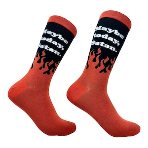 May include: A pair of crew socks featuring a black upper section with the white text "Maybe today, Satan." above a graphic of orange flames. The lower portion of the socks, including the heel and toe, is a solid orange color with a matching orange cuff.