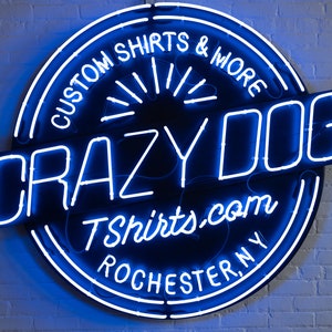 May include: A blue neon sign with a black background that reads "Crazy Dog Tshirts.com Rochester, NY" and "Custom Shirts & More".