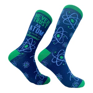 Könnte beinhalten: Ein Paar blaue Socken mit grünem Saum. Die Socken haben ein weißes Atomdesign und den Text "Vertraue niemals einem Atom, sie erfinden alles!" darauf gedruckt.