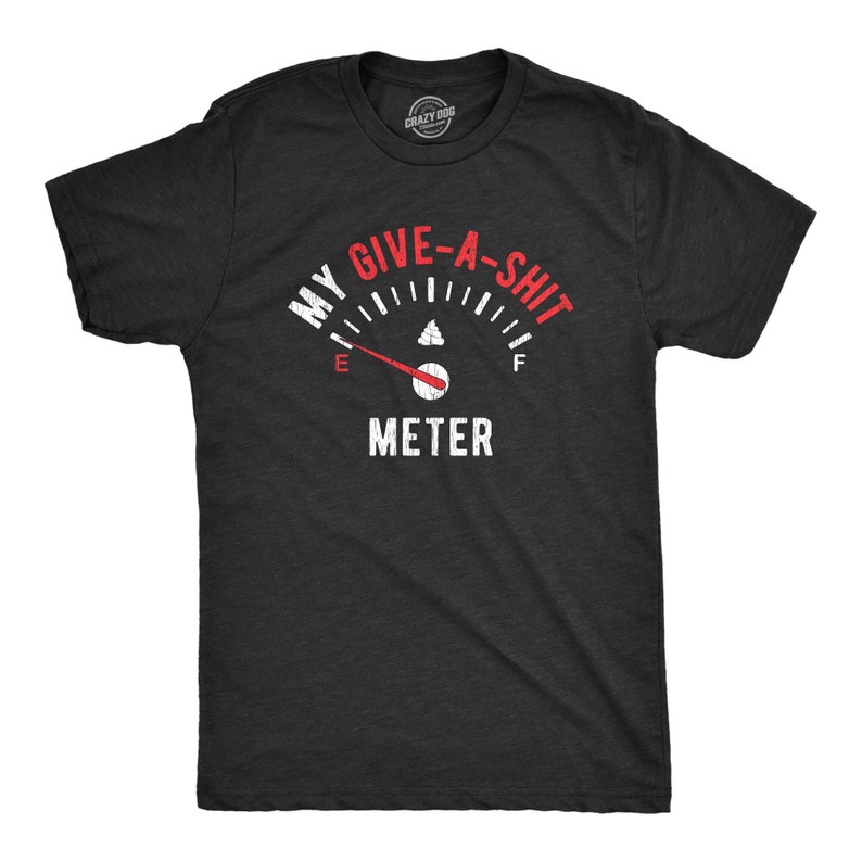 以下が含まれることがあります： 「My Give-A-Shit Meter」と書いてあるガソリンゲージの白いグラフィックがプリントされた黒いTシャツ。針は空を示しています。