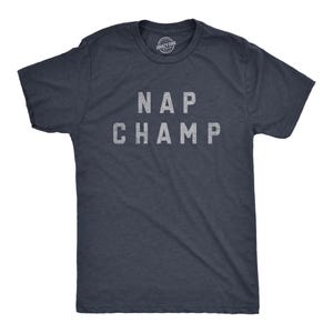 Könnte beinhalten: Ein dunkelblau meliertes Kurzarm-T-Shirt mit Rundhalsausschnitt. Auf der Brustmitte befindet sich der Schriftzug NAP CHAMP, der in einer hellgrauen Blockschrift mit Used-Look aufgedruckt ist. Der Stoff weist eine feine melierte Textur auf.