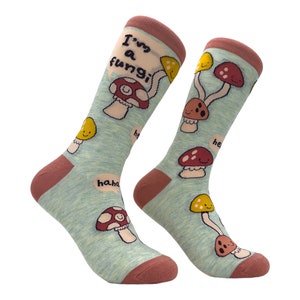 Könnte beinhalten: Ein Paar blaue und rosafarbene Socken mit einem Pilz-Design und dem Text "I'm a fungi" in einer Sprechblase. Die Socken haben ein rotes, gelbes und braunes Farbschema.