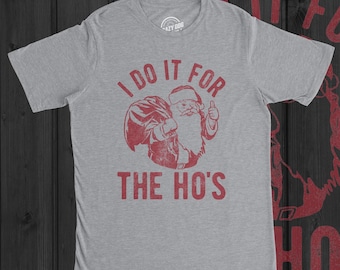 May include: A heather grey short-sleeve t-shirt featuring a red graphic of Santa Claus carrying a sack and giving a thumbs up. The text printed in red above and below the graphic reads I DO IT FOR THE HO'S in a distressed, bold, sans-serif font.