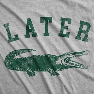 Puede incluir: Camiseta gris con un gr&aacute;fico de cocodrilo verde y la palabra "LATER" impresa en verde.