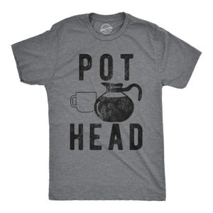 May include: A heather grey short-sleeve t-shirt featuring a black graphic print of a coffee mug and a coffee pot. The text POT HEAD is printed in a distressed black font above and below the coffee pot graphic on the front of the shirt.