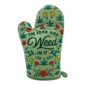May include: A sage green oven mitt featuring a repeating pattern of red roses, yellow flowers, and green cannabis leaves. The text "THE FOOD HAS Weed IN IT" is printed in dark green lettering across the center of the fabric surface.