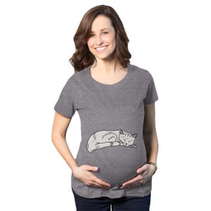 May include: A heather gray short-sleeved t-shirt featuring a black and white line art illustration of a sleeping cat centered on the front. The garment has a round neckline and a relaxed fit, providing a simple and clean aesthetic for casual wear.