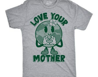 May include: A heather gray short-sleeve t-shirt featuring a dark green graphic of a smiling planet Earth character with a flower on its head, making a heart shape with its hands, accompanied by the text LOVE YOUR MOTHER in bold green letters.