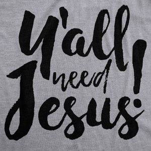 May include: A gray t-shirt with the phrase "Y'all need Jesus!" in large, black, cursive lettering. The text is centered and takes up most of the shirt's surface.