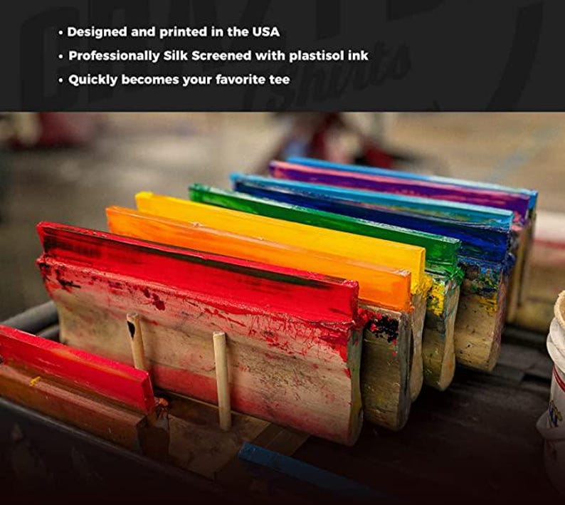 May include: A close-up of several screen printing squeegees with vibrant colors of red, orange, yellow, green, blue, and purple. The text reads: Designed and printed in the USA, Professionally Silk Screened with plastisol ink, Quickly becomes your favorite tee.
