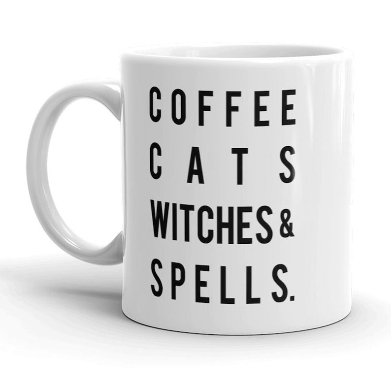 May include: White ceramic coffee mug with black text that reads "COFFEE CATS WITCHES & SPELLS."